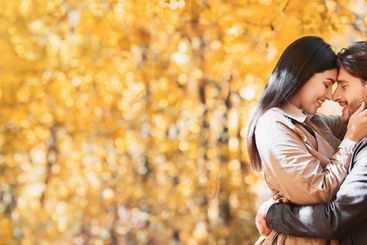 Loving man and woman cuddling while walking by golden...