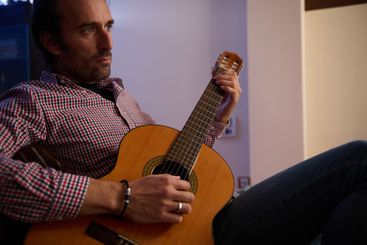 Man playing acoustic guitar indoors with focused expression