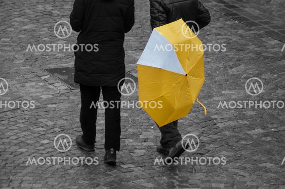 men with yellow umbrella on cobbles place in the city