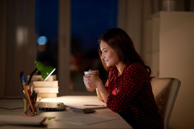 student woman with laptop and coffee at night home