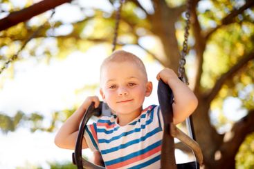 Fun, swing and portrait of boy in park with trees,...
