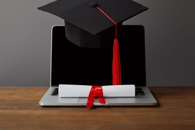 Laptop with blank screen, diploma and academic cap with...