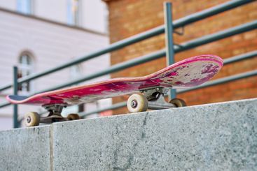 Used pink skateboard against stone wall in urban setting