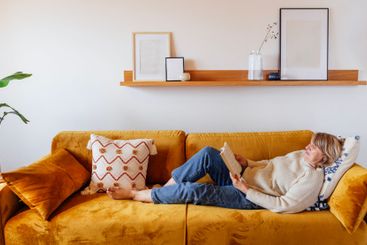 An elderly woman in casual clothes is lying on the couch...