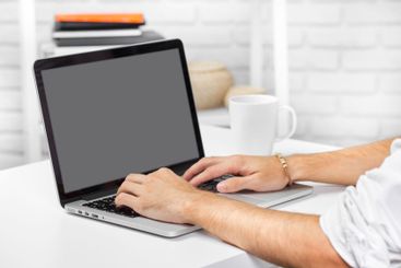 Person typing on a laptop at a white desk with a coffee...