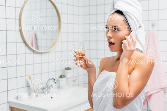 Shocked woman in towels talking on smartphone while...