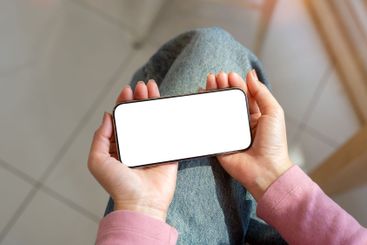 A woman in jeans sitting indoors and using her...