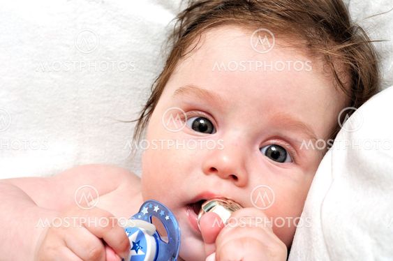Baby in bed with dummy and silver toy