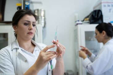 A focused nurse in a white lab coat carefully prepares a...