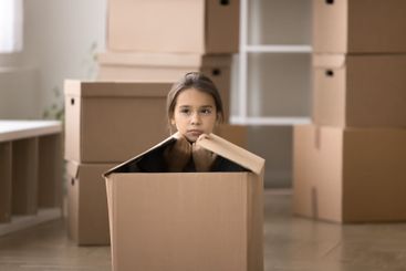 Serious pensive little girl sitting inside cardboard box