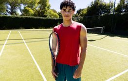 Portrait of happy fit biracial man holding tennis racket on 