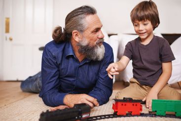 Father, child and play with toy train and joy in home or...