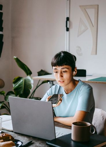 Young female freelancer talking on speaker phone while...