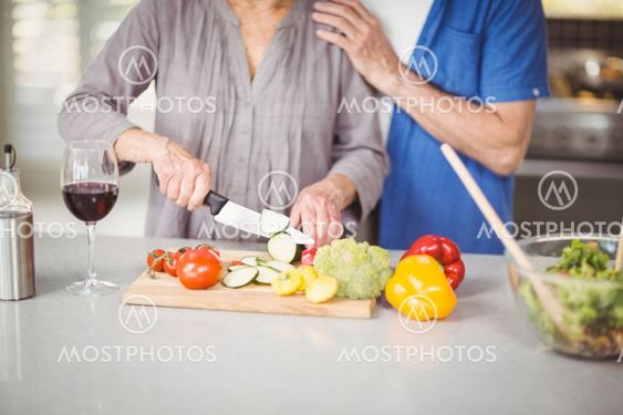 Midsection of senior man standing with woman cutting salad