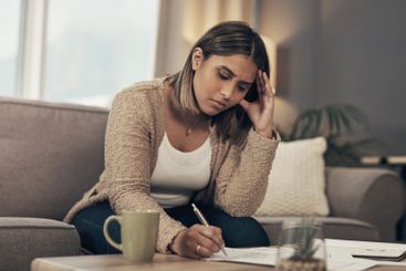 Debt, stress and woman on sofa writing finance notes...