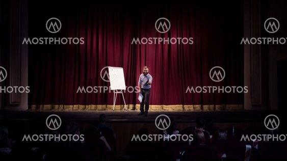 Male caucasian speaker giving presentation in hall at...