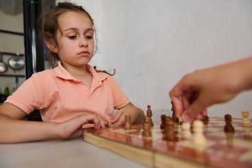Young girl playing chess with concentration at home,...