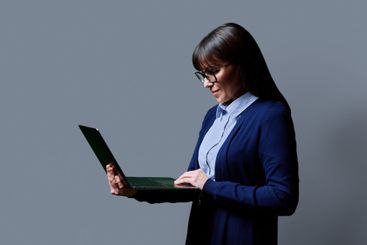 Middle aged business woman using laptop on grey background