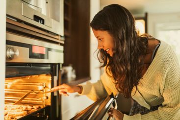 Smiling girl checking food while opening oven door