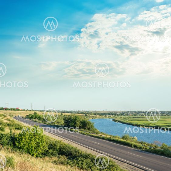 sunset in clouds over river and asphalt road