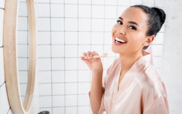 Brunette woman smiling at camera while holding toothbrush...