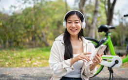 Smiling asian woman is holding a phone with finger...