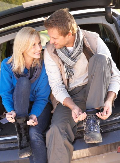 Young couple tie boots at rear of car