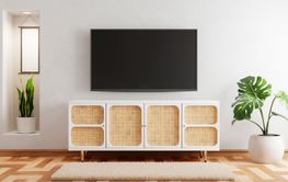 TV above wooden cabinet in modern empty room with plants...