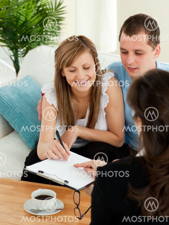 Bright young couple signing a contract sitting in their living room