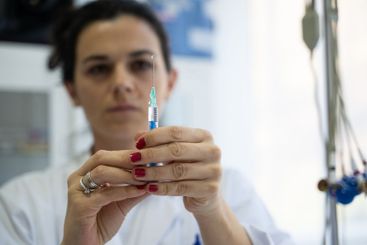 A focused nurse in a white lab coat carefully prepares a...