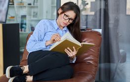 Middle aged serious woman reading book sitting on...