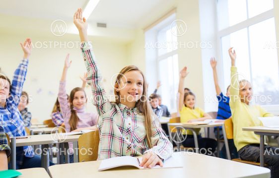 group of school kids raising hands in classroom