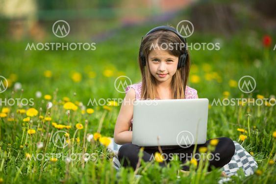 Little girl in headphones with laptop sitting on the...
