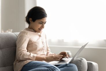 Smiling young female notebook user sit on couch type email