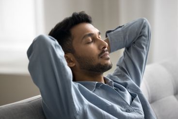 Calm young male resting on comfy couch hands behind head