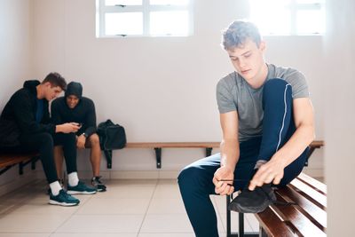 Sports, fitness and men in gym locker room tie shoes...