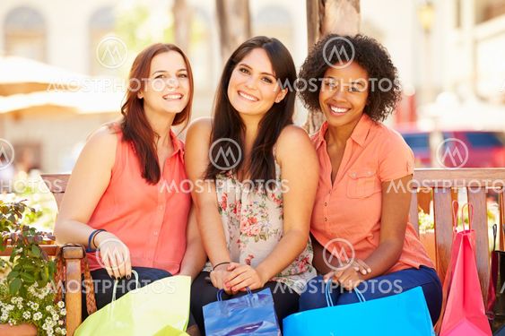 Three Female Friends With Shopping Bags Sitting In Mall