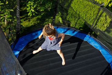 Little preschool girl jumping on trampoline. Happy funny...