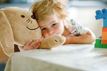 Adorable toddler girl with favorite plush bunny playing...