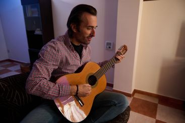 Man playing an acoustic guitar indoors wearing casual...