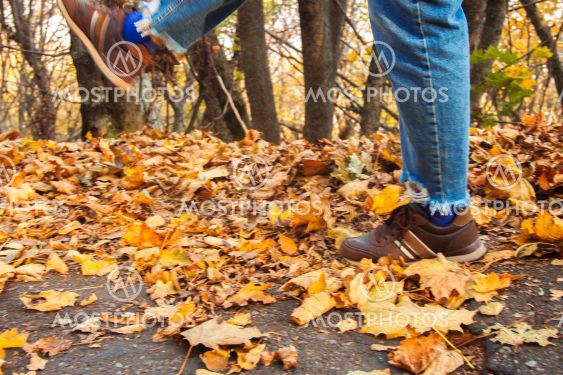 Womans leg kicks yellow autumn leaves from the ground in...