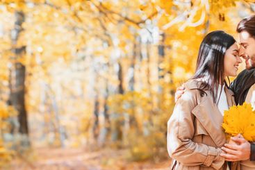Romantic lovers with bunch of golden leaves cuddling at...