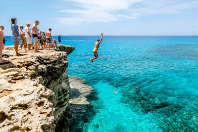  Man jumps into sea from a cliff at Cape Greco . Cyprus.