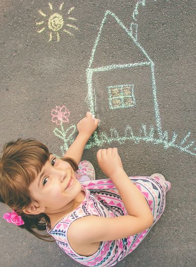 The child draws the house with chalk on the asphalt....