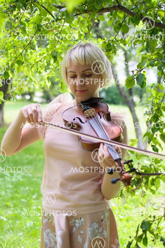 The Russian woman plays a violin in the park in the summer.