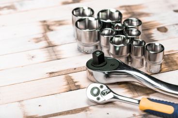 Variety of metallic tools arranged on a wooden surface,...