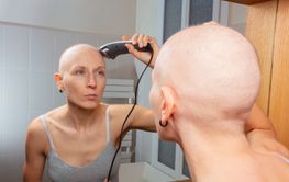 Bald woman perform self haircut with electric razor in...