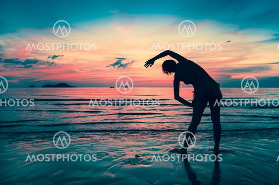 Woman doing exercises on the beach during sunset. Silhouette in twilight.