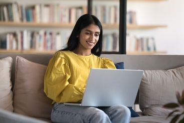 Happy young female use notebook on sofa at home office