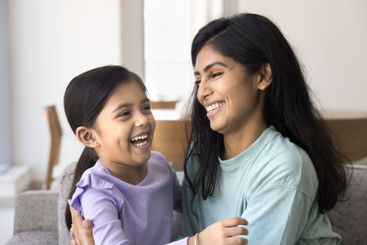 Joyful young Indian mother cuddling adorable daughter kid